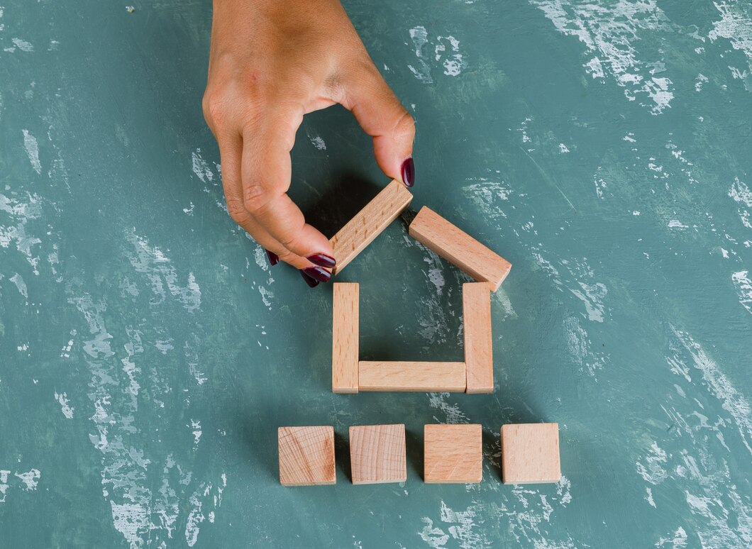 real-estate-concept-with-wooden-blocks-flat-lay-woman-making-house-model_176474-8288